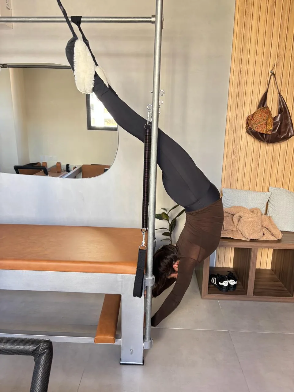 Aluna suspensa de cabeça para baixo no Cadillac, alongando e descomprimindo a coluna no estúdio Hera Pilates Clássico