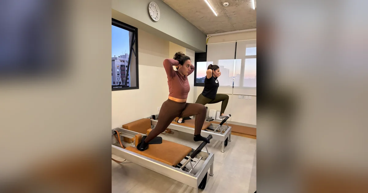 Duas alunas no reformer, mãos atrás da cabeça e tronco sustentado pelo centro, no estúdio Hera Pilates em Porto Alegre